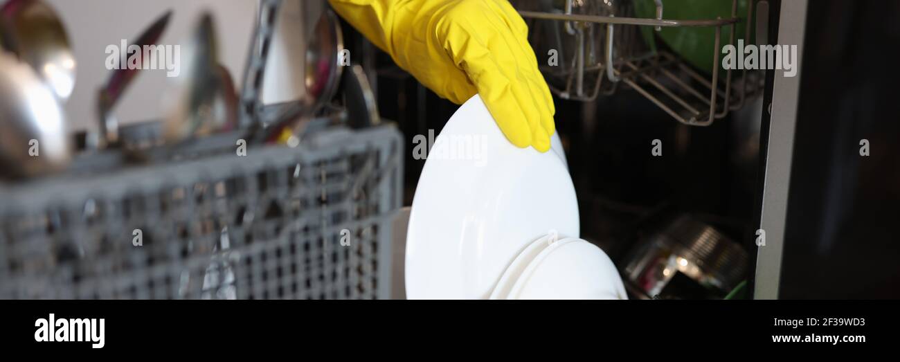 Inserire il guanto giallo ed estrarre i piatti puliti dalla lavastoviglie. Foto Stock