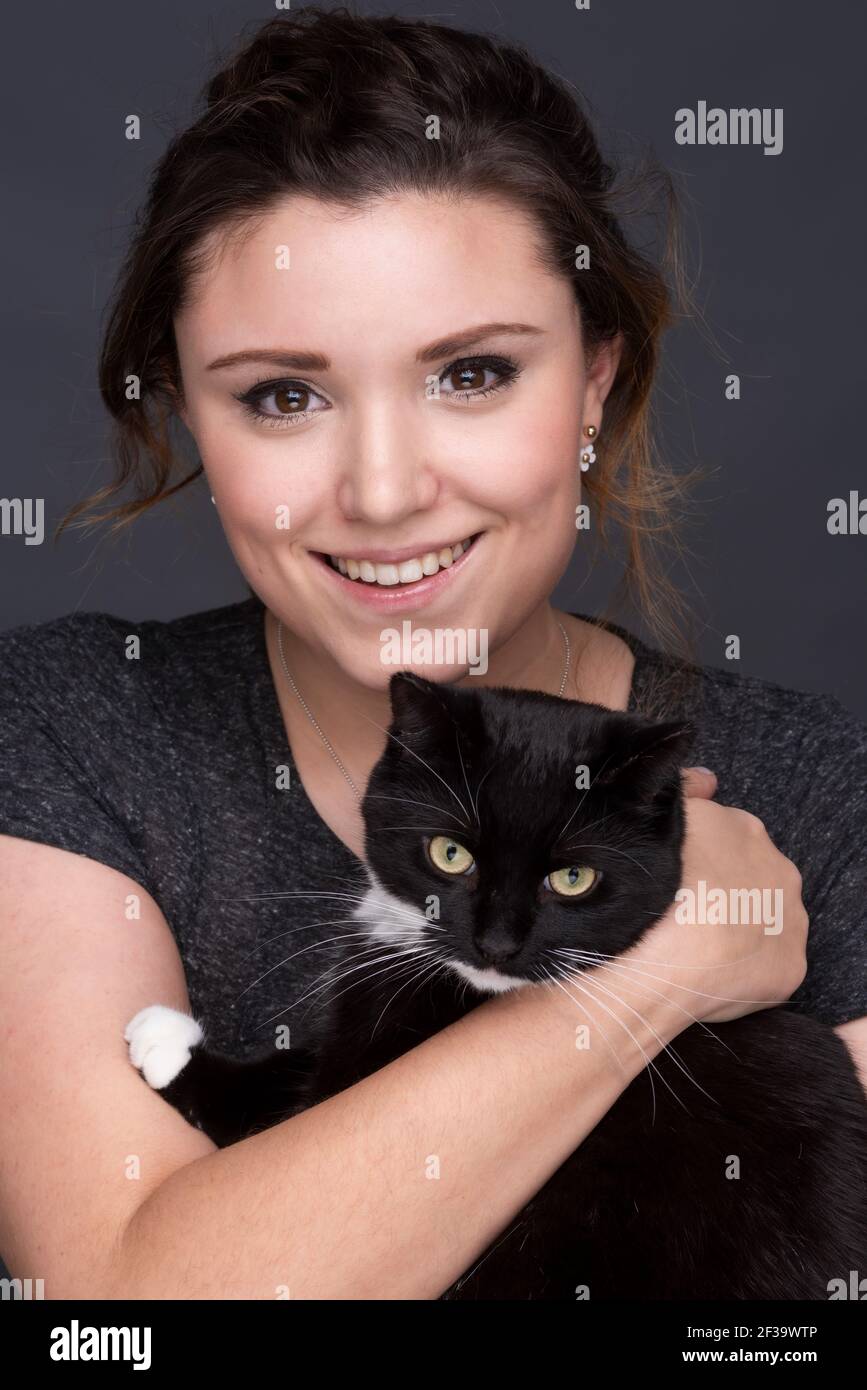 Giovane femmina adulta sorridente con un gatto bianco e nero Foto Stock