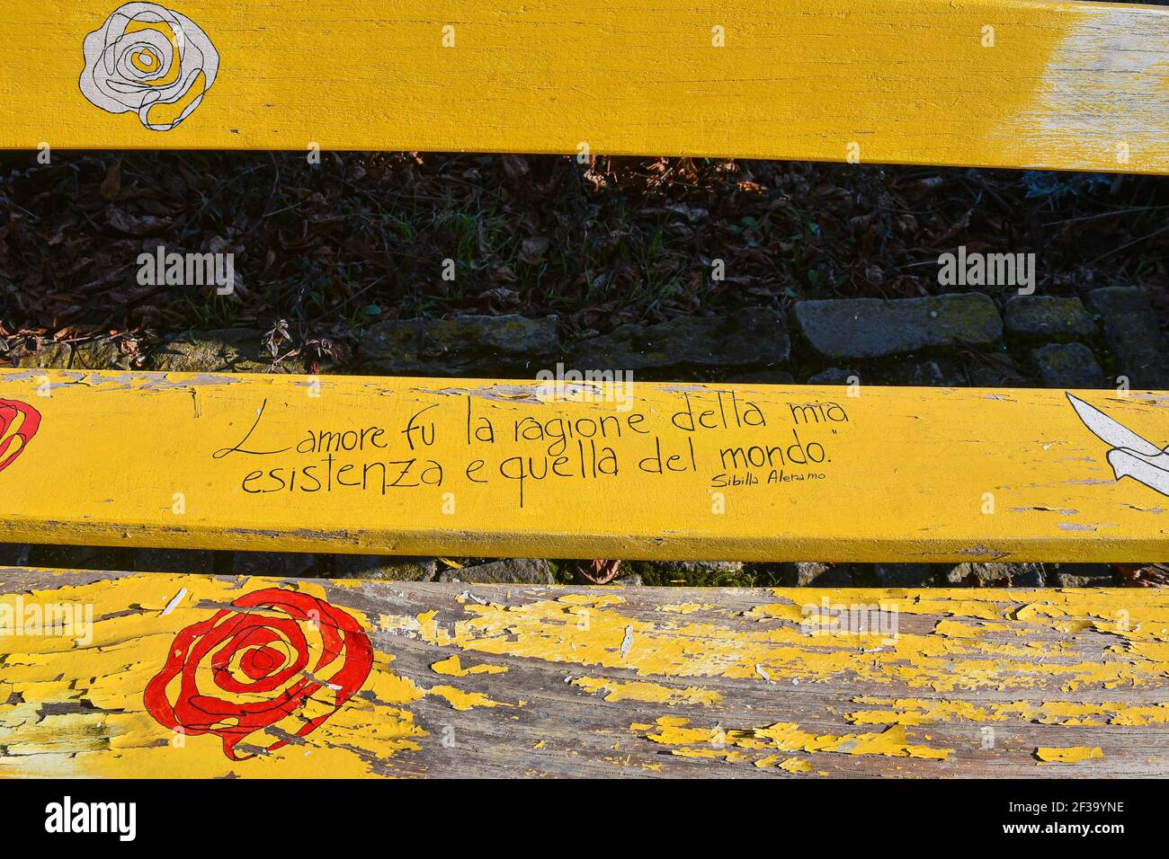 Primo piano di una panchina di parco in legno intemperie dipinta con colori brillanti e con una frase del poeta italiano Sibilla Aleramo, Serralunga d'Alba, Italia Foto Stock