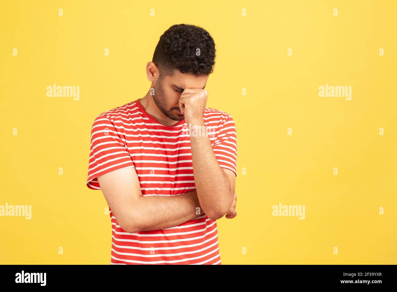 Uomo tristoso senza speranza in t-shirt a righe abbassando la testa nascondendo gli occhi, sconvolto depresso per errore, si rompe, sensazione di vergogna. Studio interno Sho Foto Stock