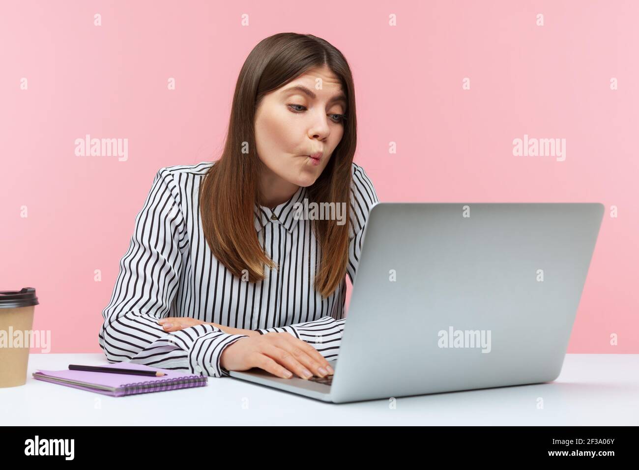 Una donna in ufficio che guarda lo schermo del computer portatile con pesci umorosi faccia grimace, faccia imbrogliante che parla in videochiamata, comunicazione online. Indù Foto Stock