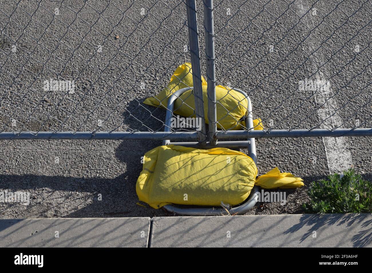 Due sacchi di sabbia completamente gialli sotto una recinzione di metallo vicino un marciapiede all'esterno Foto Stock