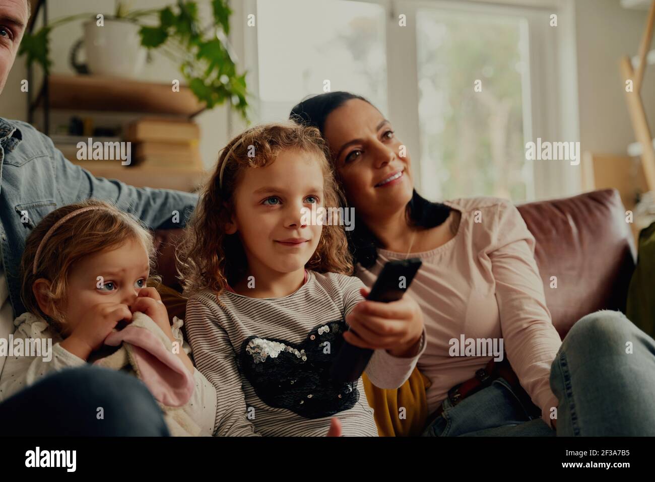 Ragazza felice che guarda la televisione che controlla mentre controlla il telecomando e seduto con la famiglia sul divano Foto Stock