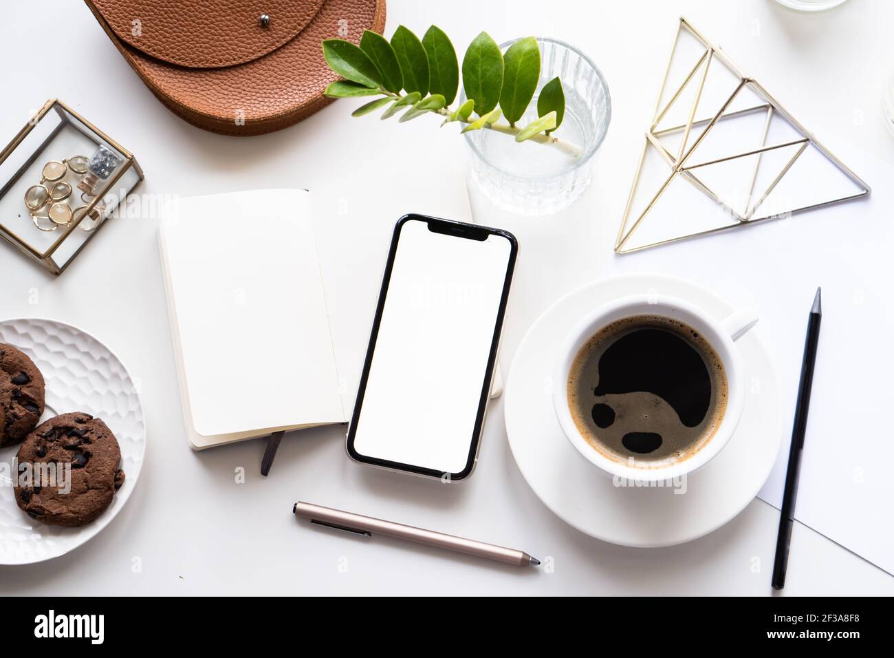 Piano da tavolo bianco per l'ufficio domestico con mock-up per smartphone, tazza da caffè e blocco note Foto Stock