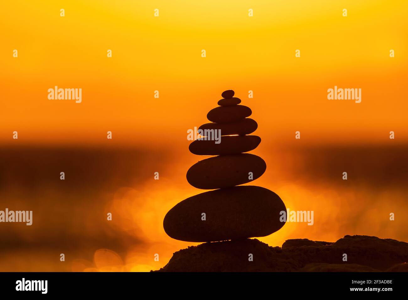 Profilo a piramide di ciottoli bilanciato sulla spiaggia. Astratto caldo tramonto bokeh con Mare sullo sfondo. Pietre Zen sulla spiaggia di mare, meditazione, spa Foto Stock