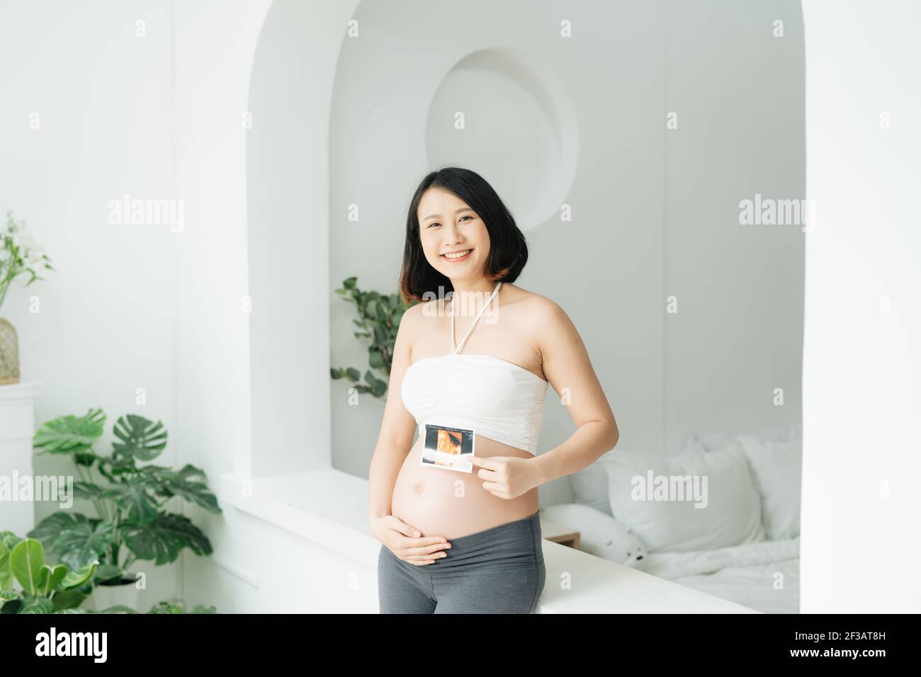 La donna incinta tiene una foto ecografica sul ventre in vita camera Foto Stock