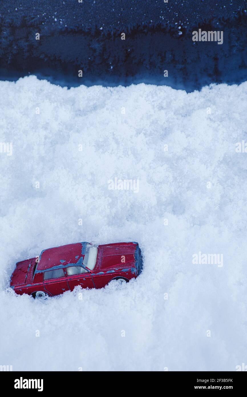 Auto giocattolo rossa bloccata in neve profonda drift Blizzard. Concetto di intrappolato, cambiamento climatico, condizioni atmosferiche estreme Foto Stock