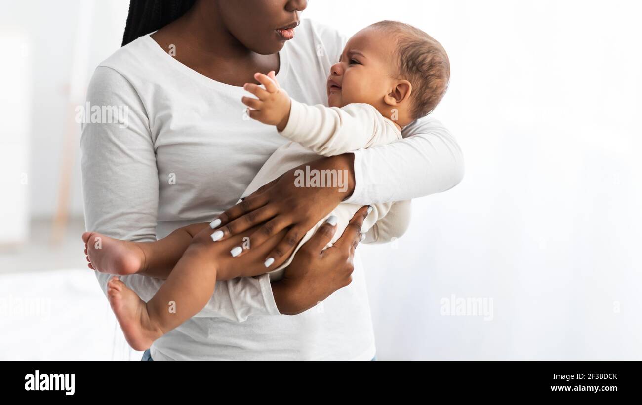 Ritratto di madre nera che tiene il bambino piangente sulle mani Foto Stock