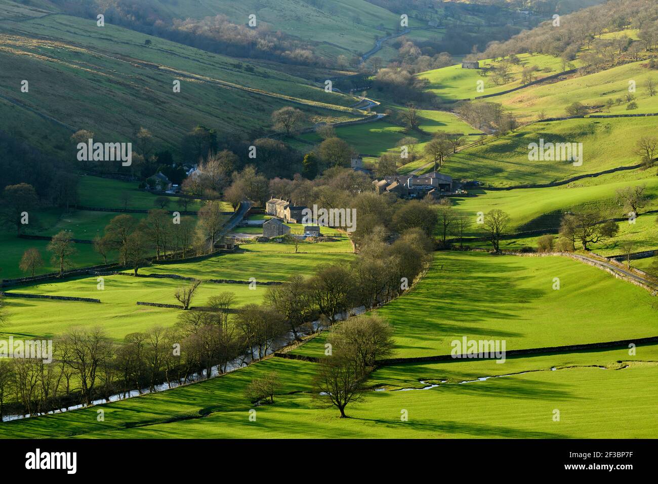 Picturesque Dales village (cottages & farms) & River Wharfe, nestling by hills & hillsides in steep-sided valley - Hubberholme, Yorkshire, England, UK Foto Stock