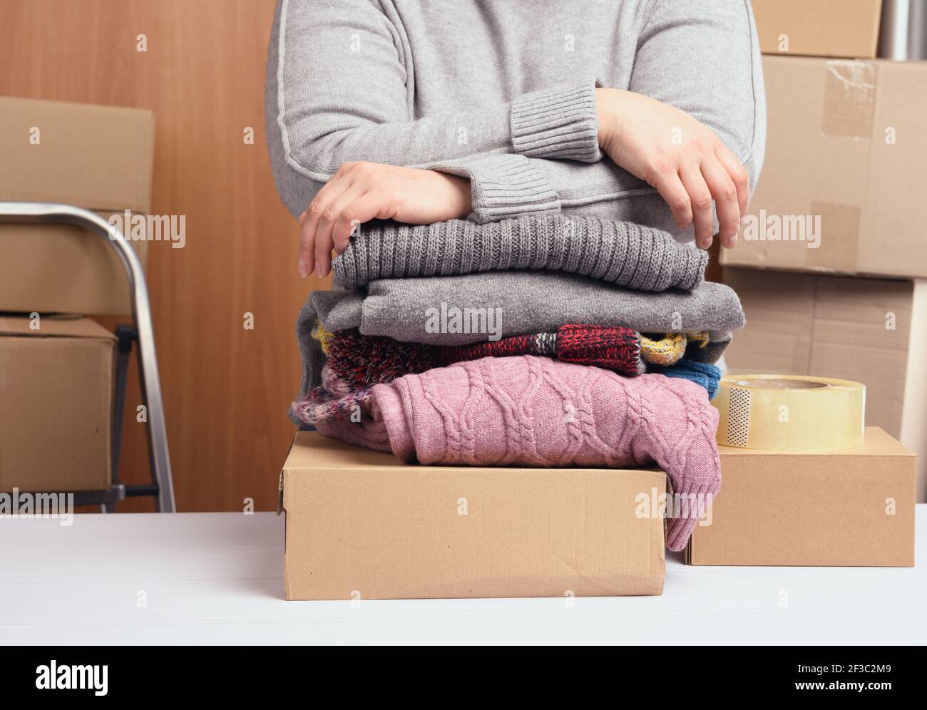 donna in un maglione grigio sta imballando i vestiti in una scatola, il concetto di assistenza e di volontariato, in movimento. Vendere cose non necessarie Foto Stock