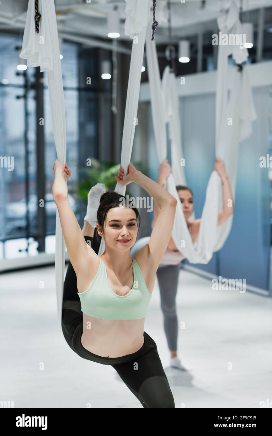 donna sorridente che si strizza con amache da yoga aeree nel centro fitness Foto Stock