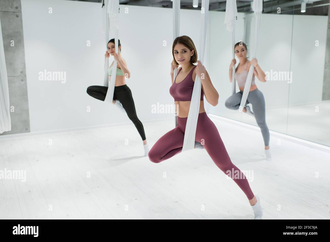 tre giovani donne si riscaldano su amache per yoga aeree centro fitness Foto Stock