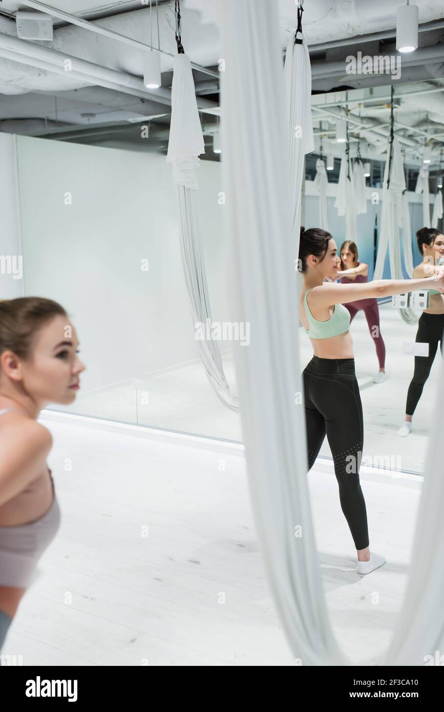 le giovani donne si riscaldano vicino alle amache da yoga aeree nel centro fitness, in primo piano sfocato Foto Stock