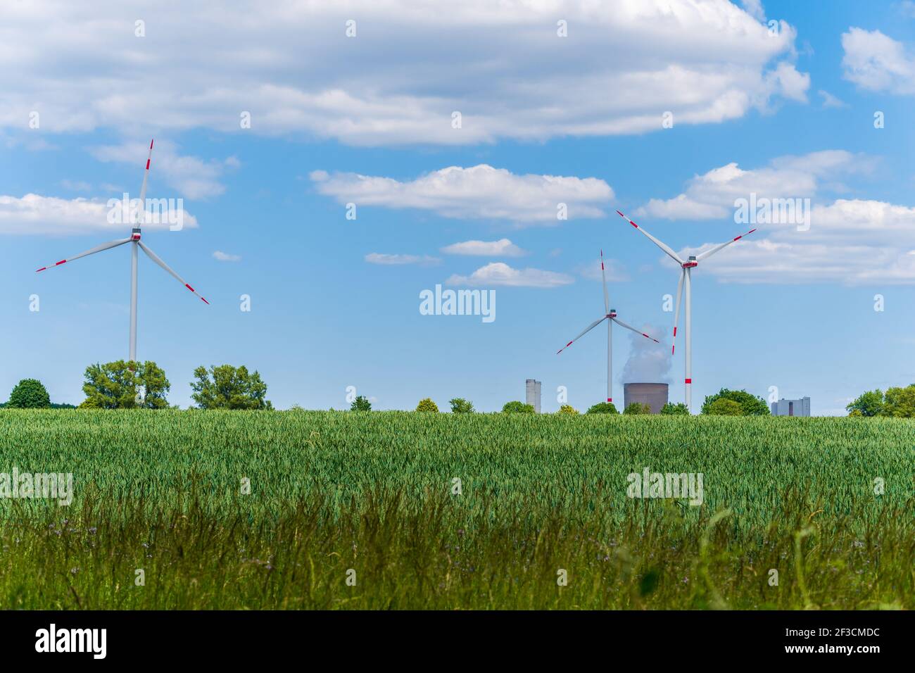 Turbine eoliche e centrale elettrica con camino fumante in splendido paesaggio con lussureggiante campo di grano agricolo e cielo blu con nuvole. Foto Stock