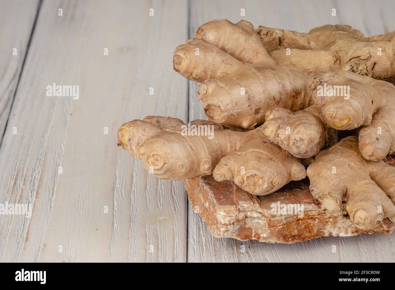 Zenzero fresco, leggero e sano su sfondo bianco di legno Foto Stock