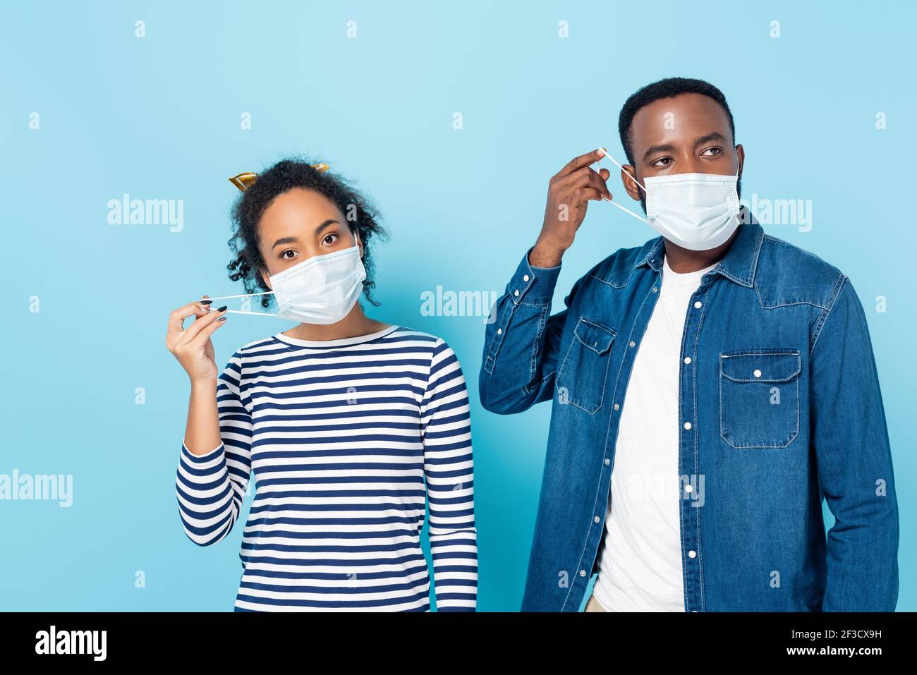 giovane coppia afroamericana che mette su maschere mediche su blu Foto Stock