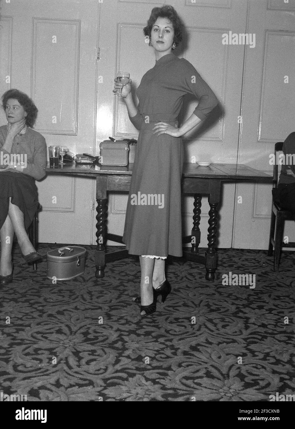 1957, storica, elegante giovane donna in un elegante vestito dell'epoca in un ufficio festa in una sala con un bicchiere di vino, Victoria Hotel, Leeds, Inghilterra. REGNO UNITO. Foto Stock