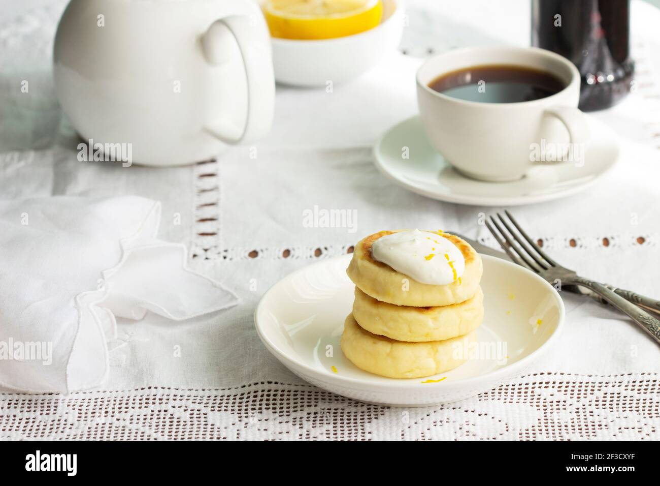 Frittelle al formaggio con panna acida e scorza di limone, servite con tè. Foto Stock