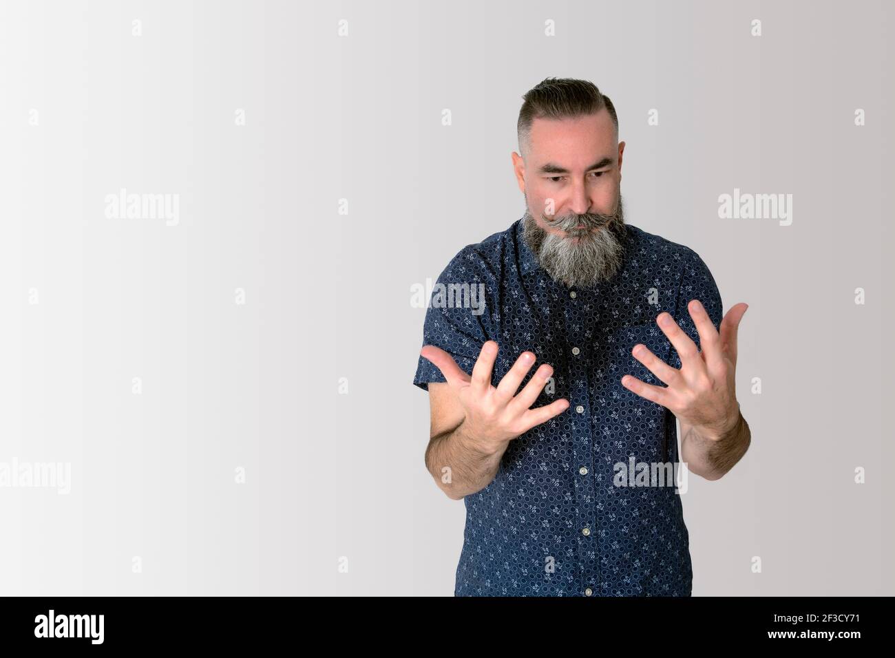 Hipster con una grande barba mezza bianca di circa 40/45 anni caucasica, guardando le mani sorpresi e ponderati. Foto Stock