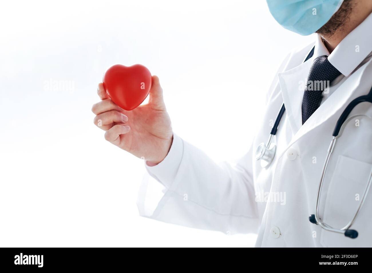 il medico in una maschera protettiva tiene un cuore rosso nelle mani. Foto Stock