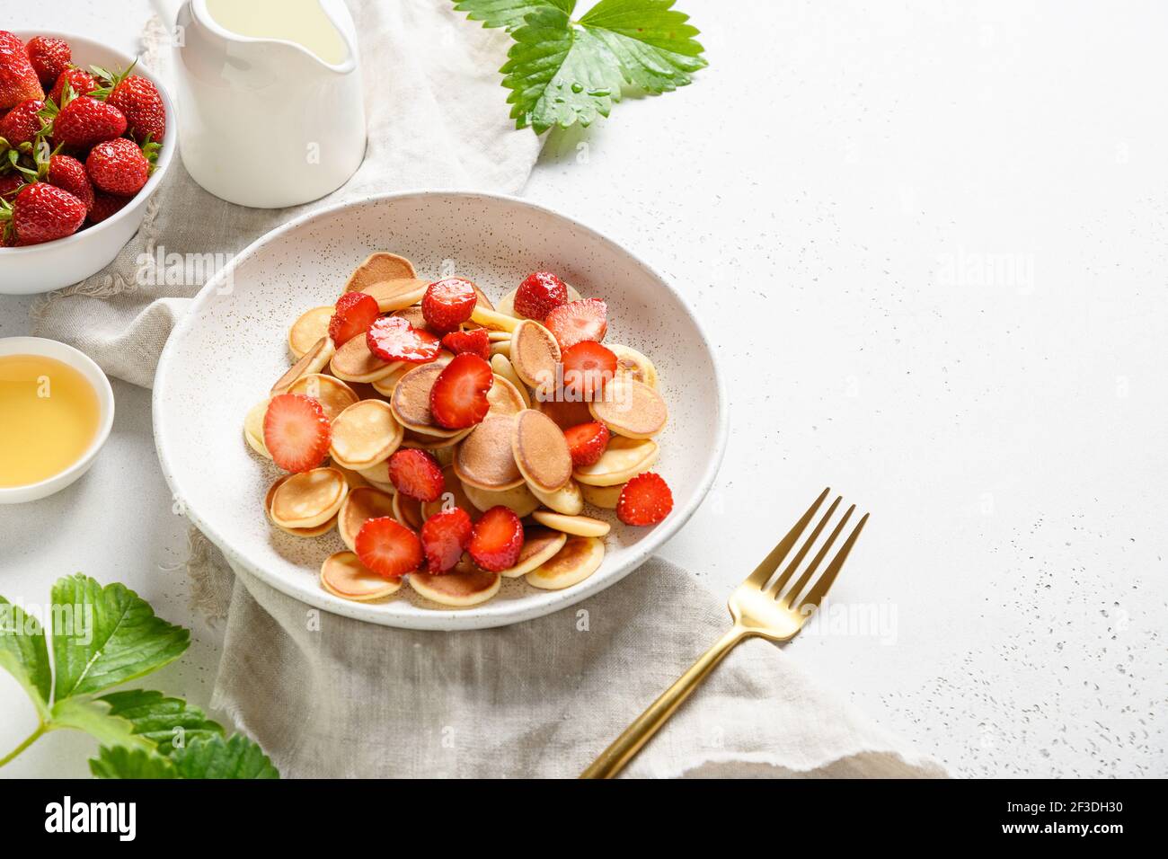Colazione estiva con minuscoli pancake e fragola fresca su tavola bianca. Spazio di copia. Primo piano. Foto Stock
