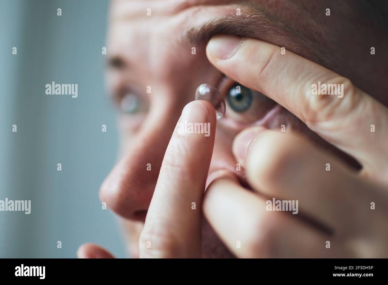 Giovane uomo che mette la lente a contatto sull'occhio. Temi vista e routine quotidiana. Foto Stock