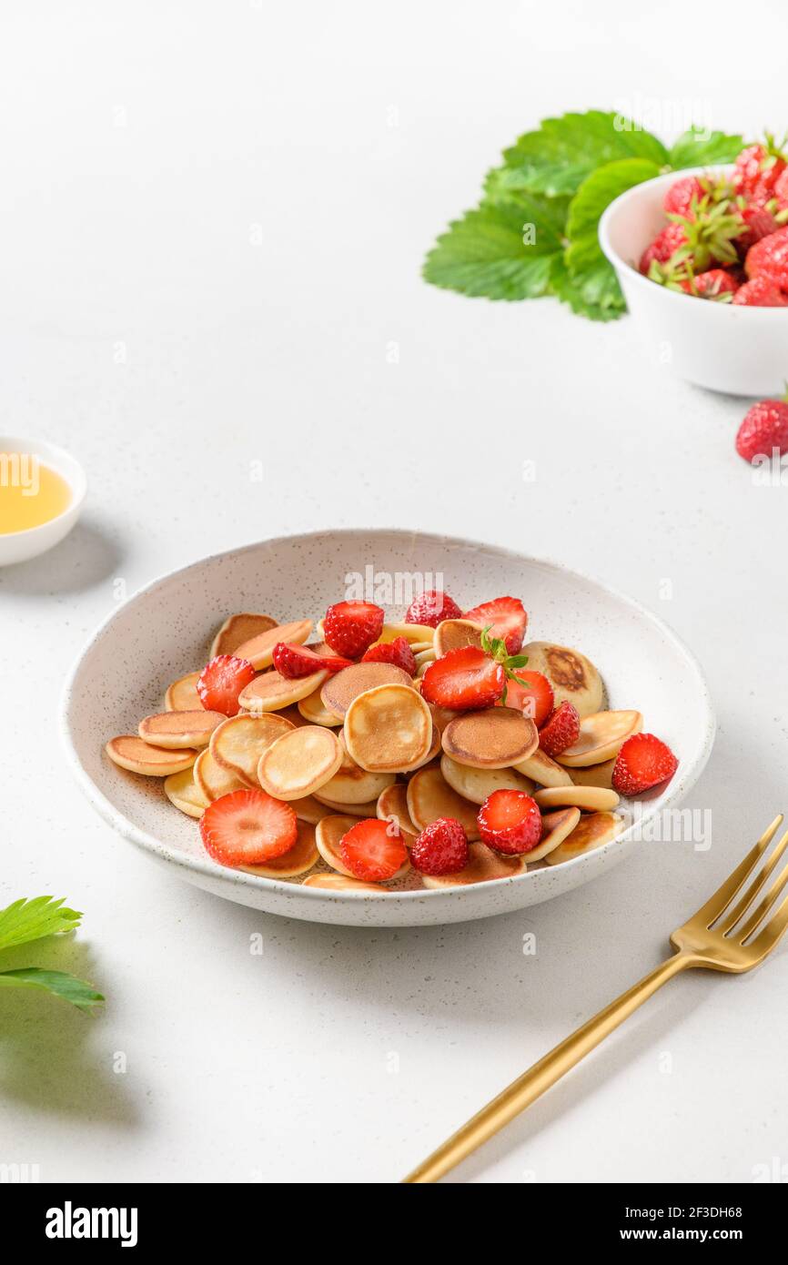 Colazione estiva con minuscoli pancake e fragola fresca su tavola bianca. Primo piano. Formato verticale. Foto Stock
