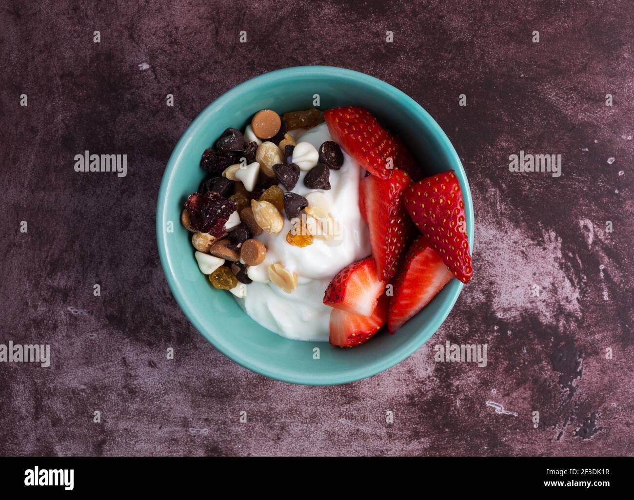 Vista dall'alto di una ciotola con yogurt greco puro e un mix di dolci e fragole su un piano di un marronone. Foto Stock