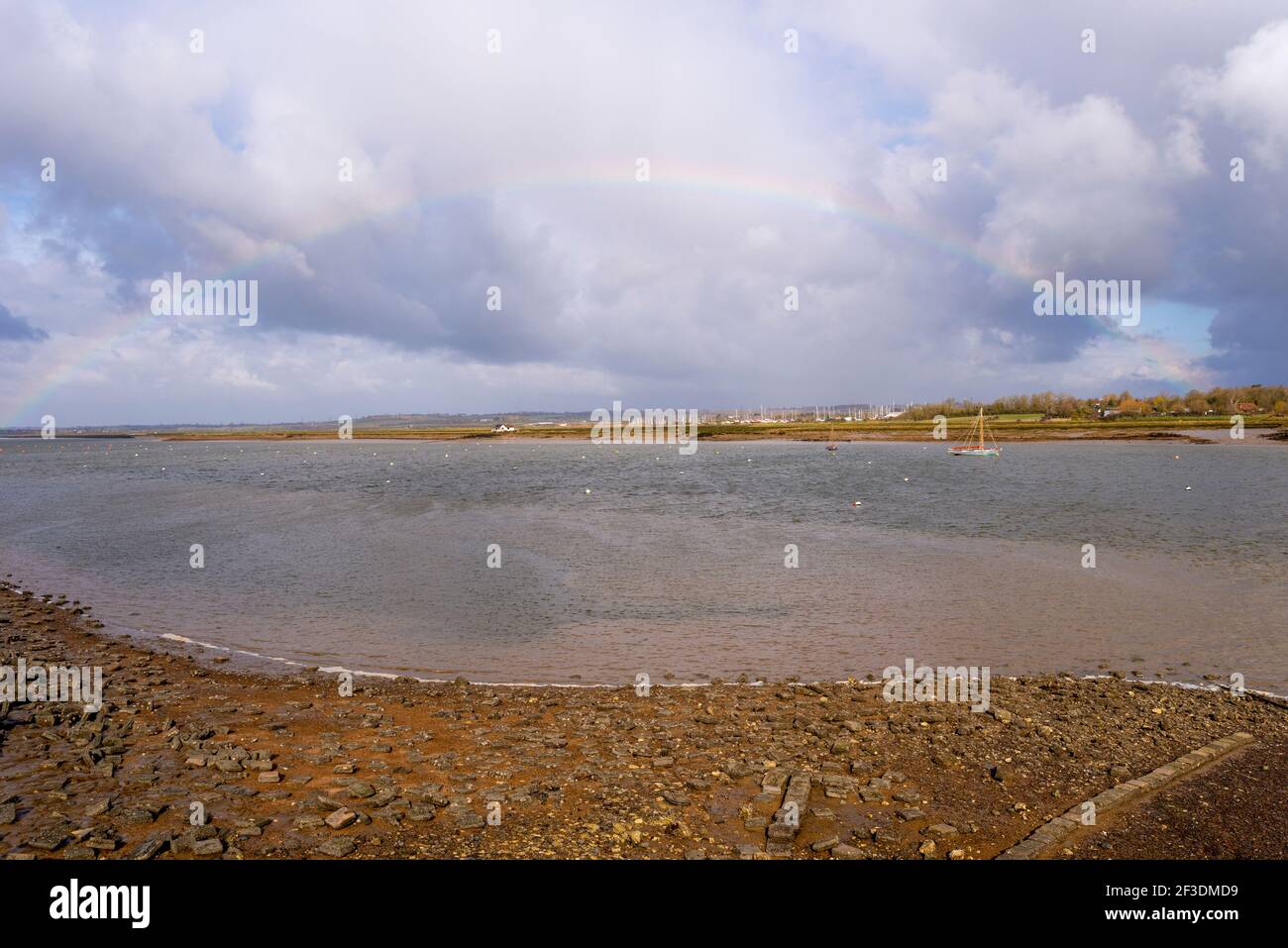 Rainbow sul fiume Crouch guardando verso North Fambridge, Essex, UK. Cielo pesante. Fiume a bassa marea che mostra il litorale con pietra Foto Stock