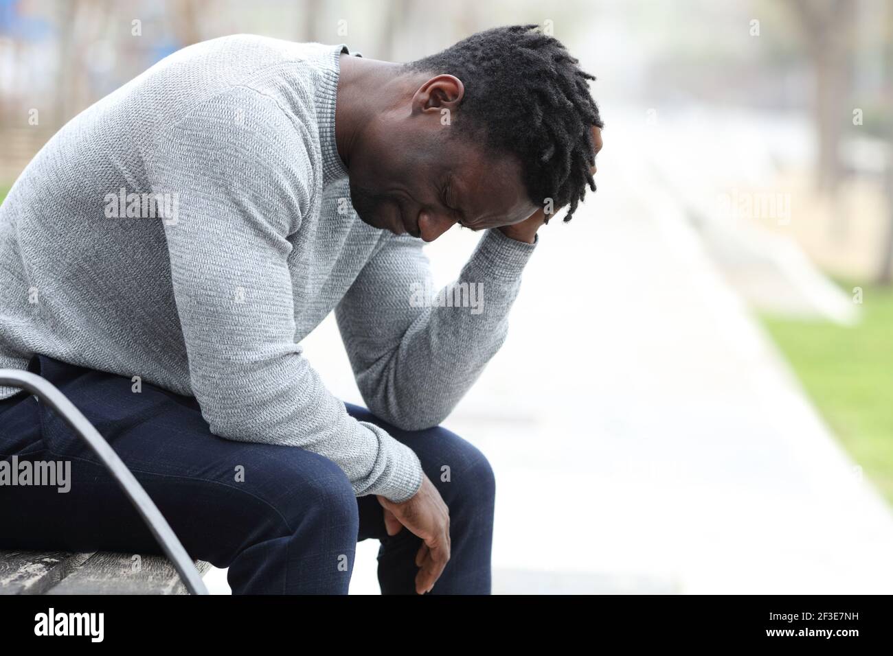 Profilo di un triste uomo nero che si lamenta da solo seduto una panchina in un parco Foto Stock