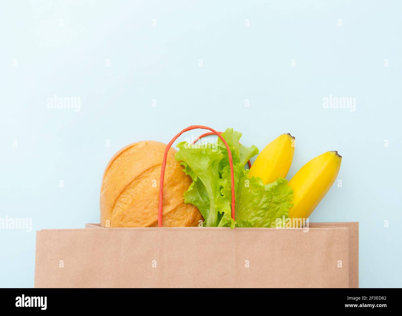 Sacchetto di carta con cibo: Foglie verdi di insalata, pane e banana. Stendere su sfondo blu, vista dall'alto Foto Stock