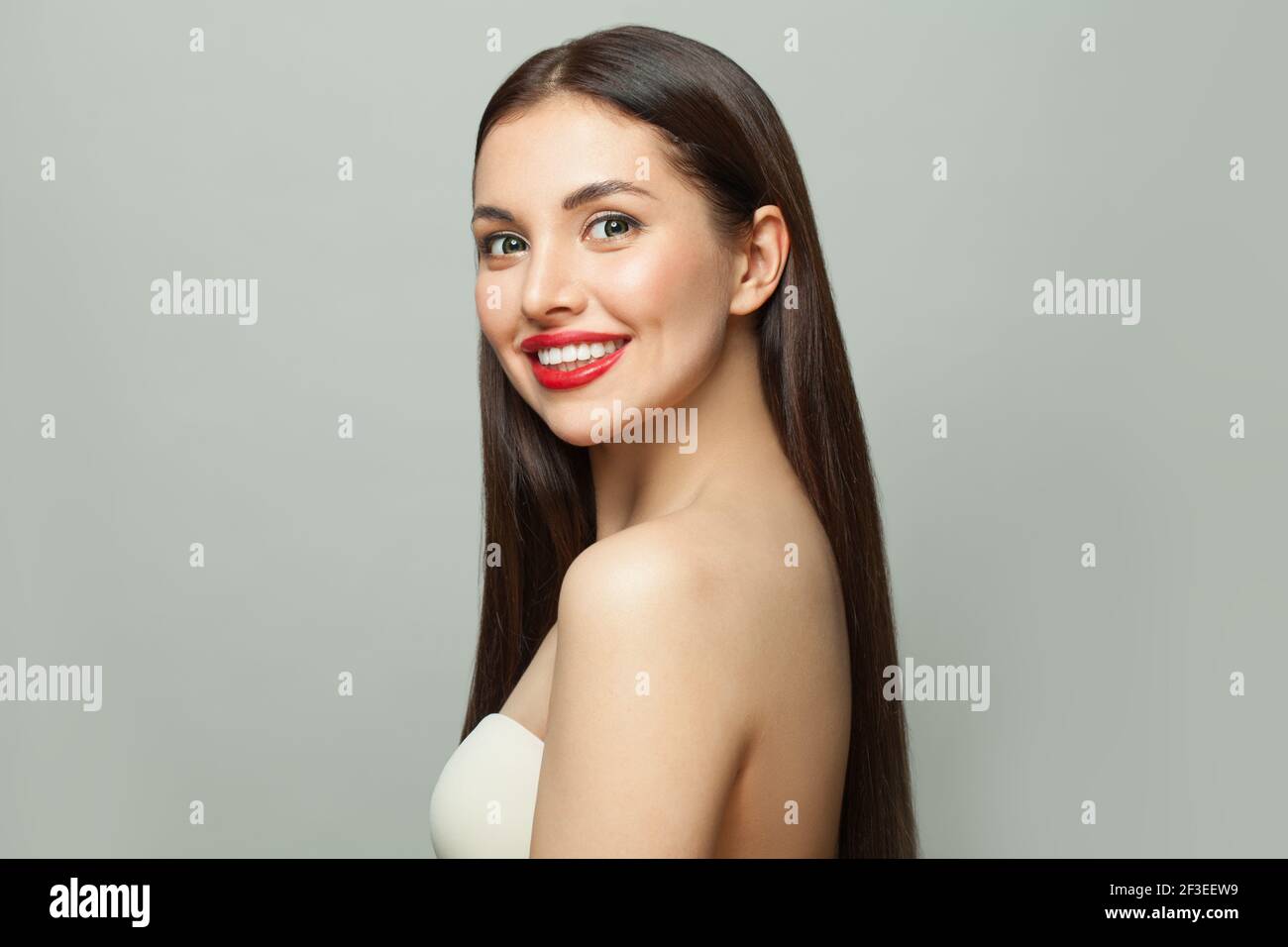 Giovane donna felice brunetta con pelle chiara e lunga lucida capelli lisci su sfondo bianco Foto Stock