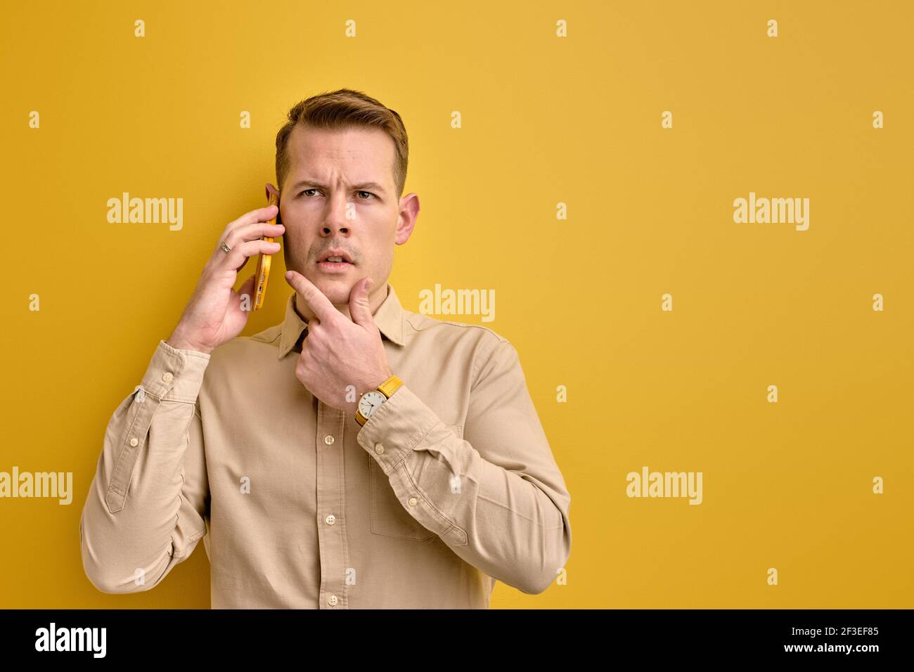 Ne ho idea. Uomo che condivide idee con il partner commerciale mentre si parla al telefono, stare pensando alla domanda, isolato su sfondo giallo Foto Stock