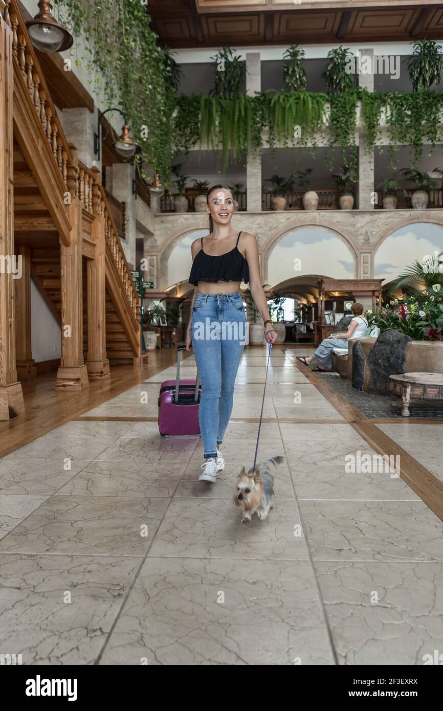 Donna con valigia e Yorkshire Terrier a piedi nella lobby di hotel di lusso durante la vacanza Foto Stock