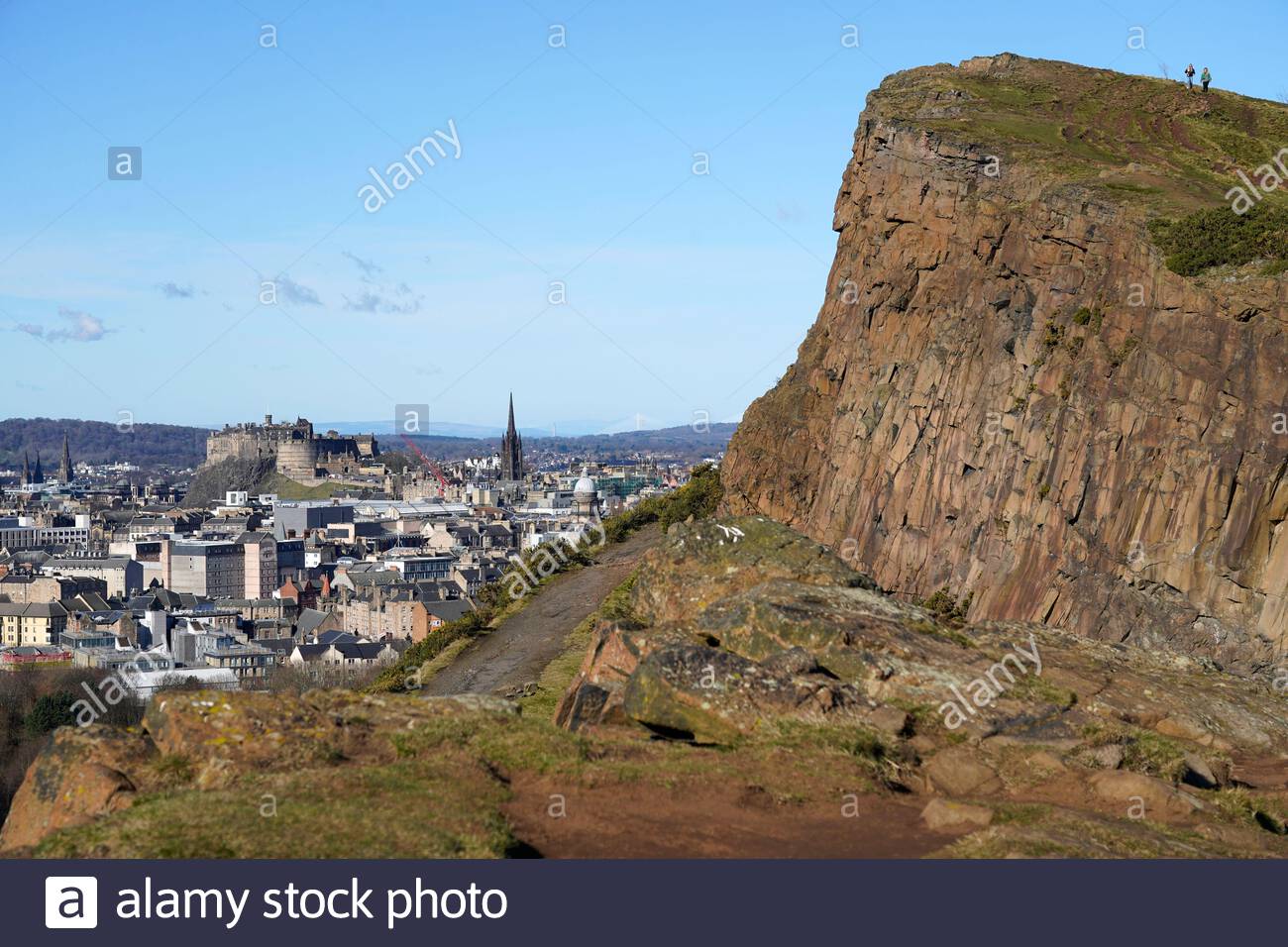 Le persone che si godono il sole e all'aperto in Holyrood Park. Da Salisbury Crags si può ammirare il Castello di Edimburgo e i tetti del centro città, Edimburgo, Scozia Foto Stock