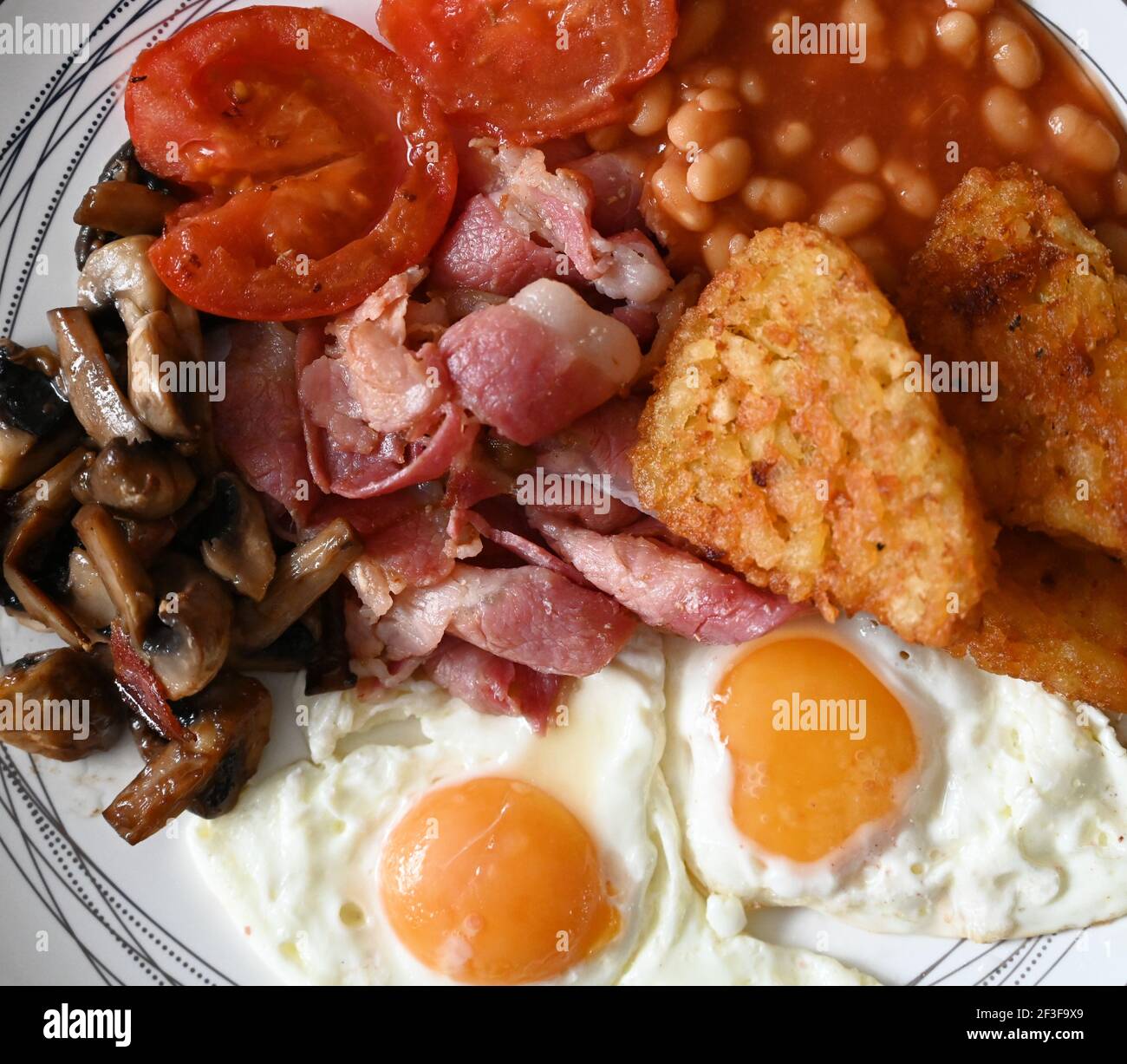 Colazione inglese tradizionale - piatto con uova fritte, fagioli, funghi, pancetta, crocchette di patate e pomodori Foto Stock