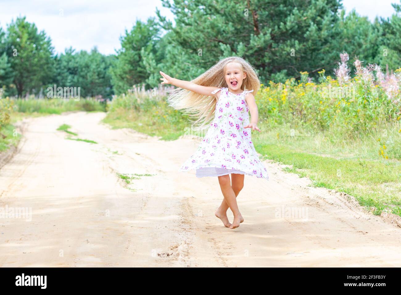 Una ragazza con lunghi capelli ricci biondi sta ballando, girando su una strada forestale. Foto Stock