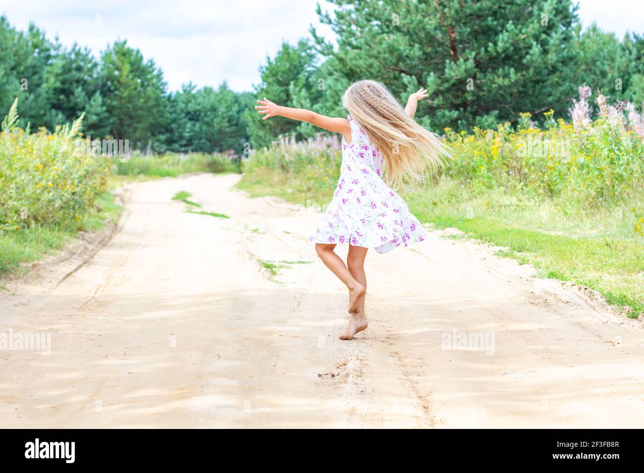Una ragazza con lunghi capelli ricci biondi sta ballando, girando su una strada forestale. Foto Stock