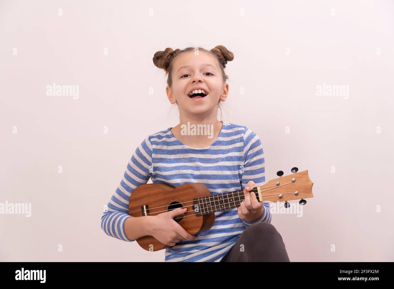 La ragazza canta e suona l'ukulele. Il bambino ride, si pone per la macchina fotografica e gode la musica. Imparare a giocare ukuleles Foto Stock