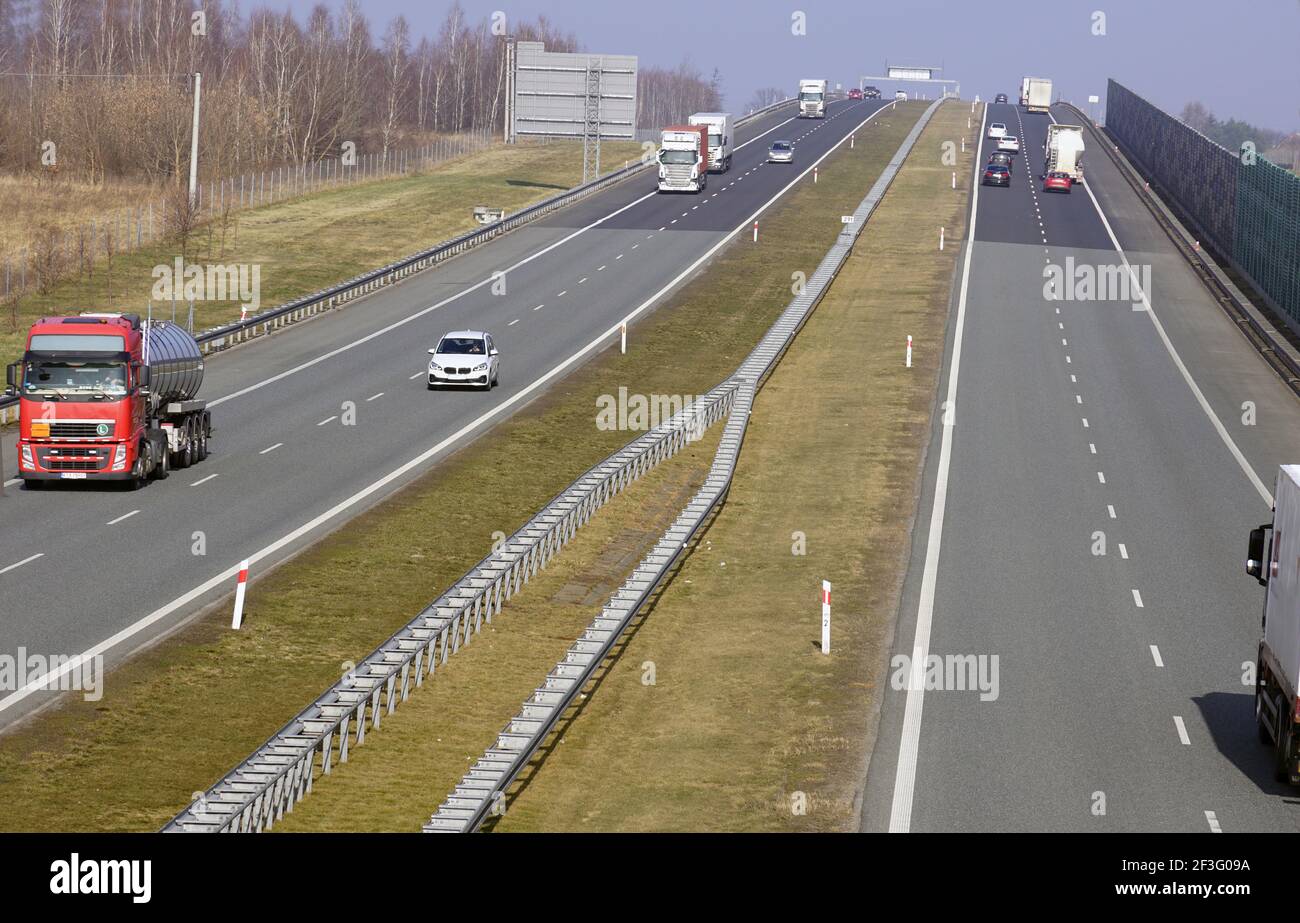 Veicoli che viaggiano in autostrada. Barriere fonoassorbenti visibili che separano l'autostrada dall'area residenziale. Foto Stock