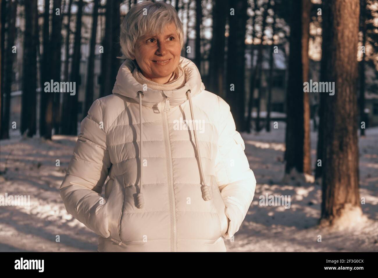 Ritratto di una felice donna di mezza età in inverno in un parco cittadino innevato al tramonto. Vacanza invernale e concetto di viaggio. Foto Stock