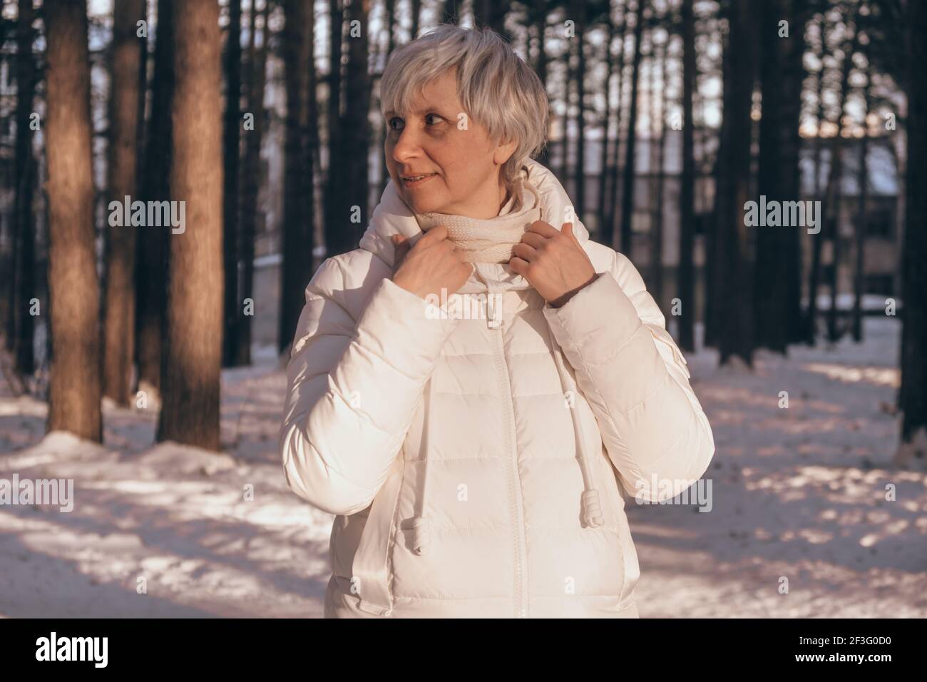 Ritratto di una felice donna di mezza età in un parco cittadino innevato all'ora del tramonto. Sorride e guarda via. Vacanza invernale e concetto di viaggio. Foto Stock