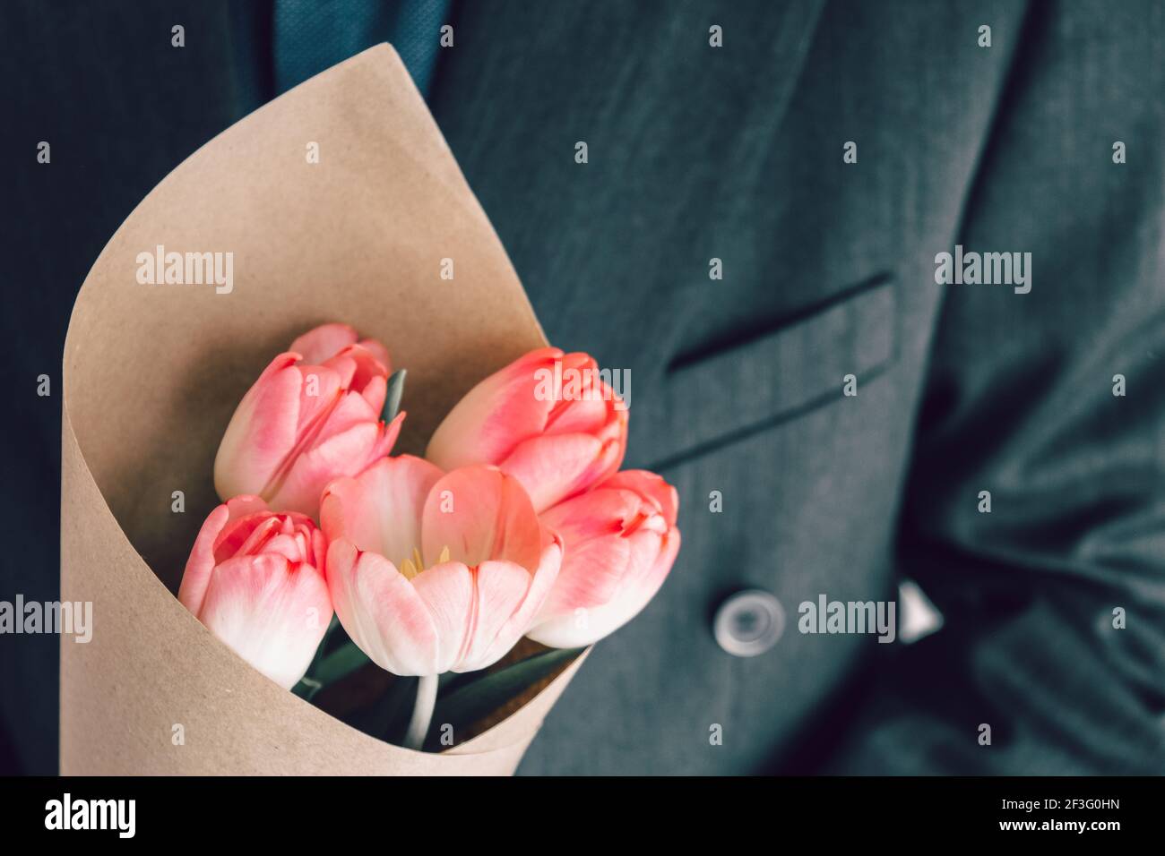 Uomo elegante che tiene un bouquet di tulipani rosa avvolti in carta artigianale. Sorpresa per la tua amata donna. Concetto di fuga romantica. Messa a fuoco selettiva. Foto Stock