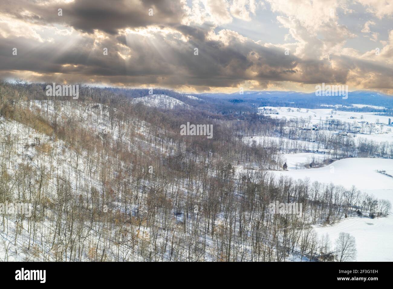 Un cielo dinamico con raggi di sole sopra un paesaggio invernale innevato nella contea di Jackson, IN. La neve che soffia appare in due aree all'orizzonte lontano. Foto Stock