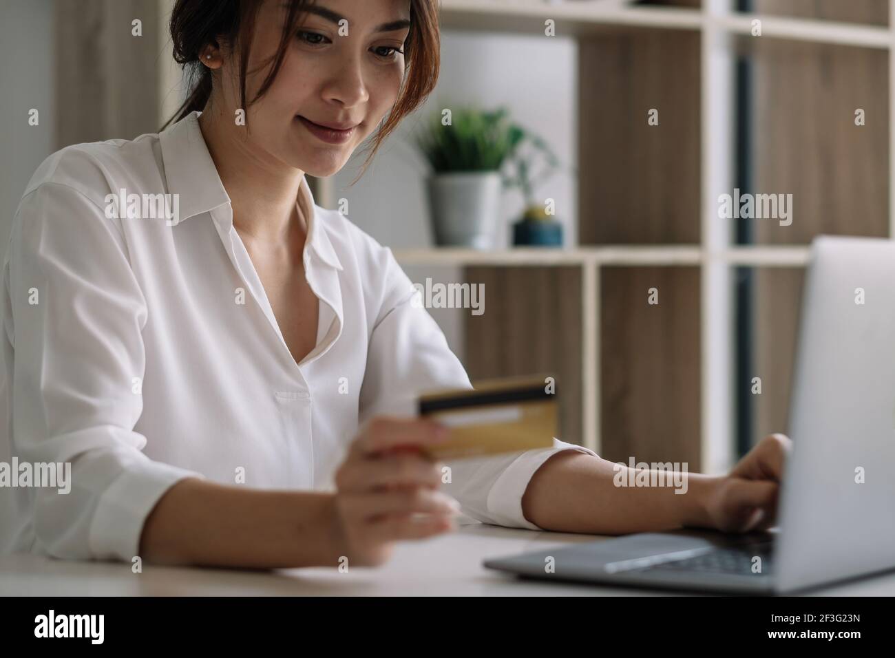 Donna felice che usa il computer portatile e la carta di credito per lo shopping online a casa. Foto Stock