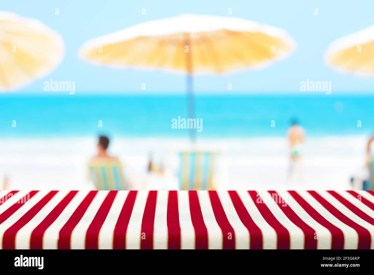 Tavolo coperto con tovaglia a righe su sfondo di spiaggia sfocata - picnic e concetti di festa Foto Stock