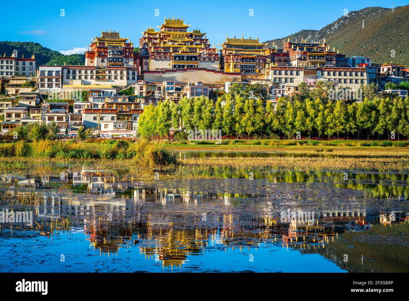Splendida vista panoramica del monastero di Ganden Sumtseling con riflessi d'acqua Al tramonto e cielo blu a Shangri-la Yunnan Cina Foto Stock