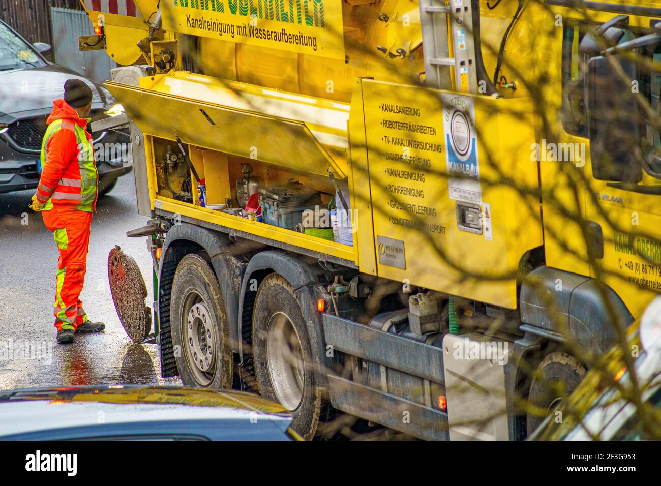 Il pulitore di scarico è in piedi davanti ad una copertura aperta del tombino, facendo il suo lavoro ad un giorno piovoso su una strada. Foto Stock
