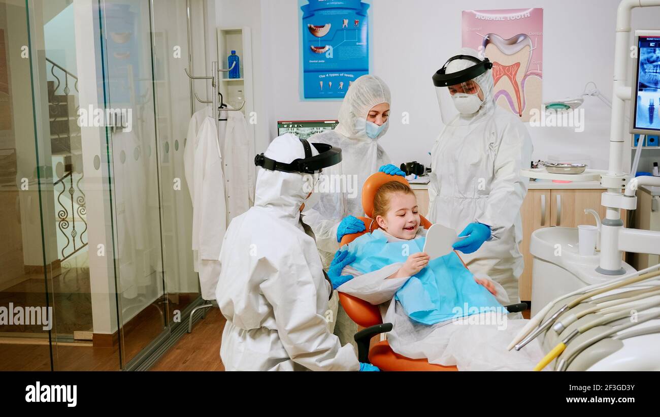 Medico dentista in tuta trattamento dentale di finitura del bambino in clinica  stomatologica durante la pandemia globale. Team medico che indossa tuta  protettiva, maschera di protezione del viso e guanti che esaminano