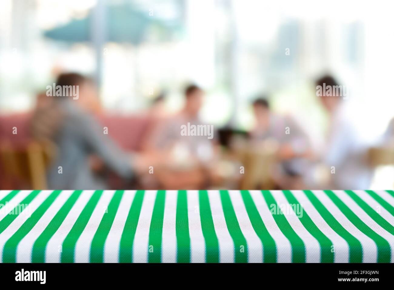 Tavolo coperto con tovaglia striata su sfondo sfocato di persone in caffetteria - possono essere utilizzati per montaggio e. mostra alimenti o prodotti Foto Stock